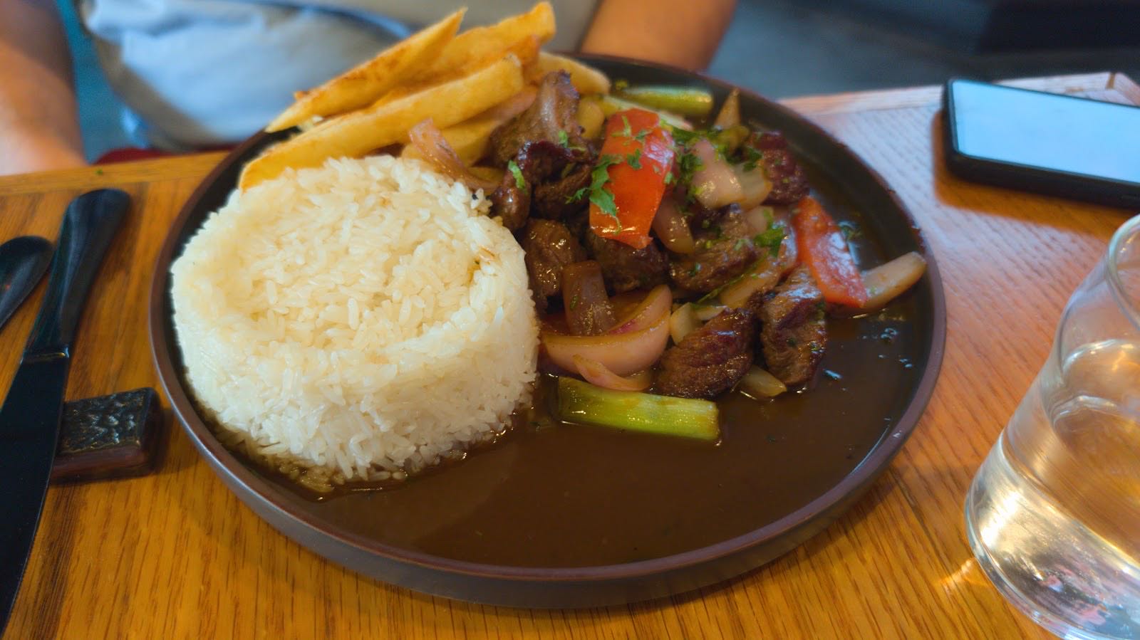 Lomo saltado with rice and fries served in a dark bowl